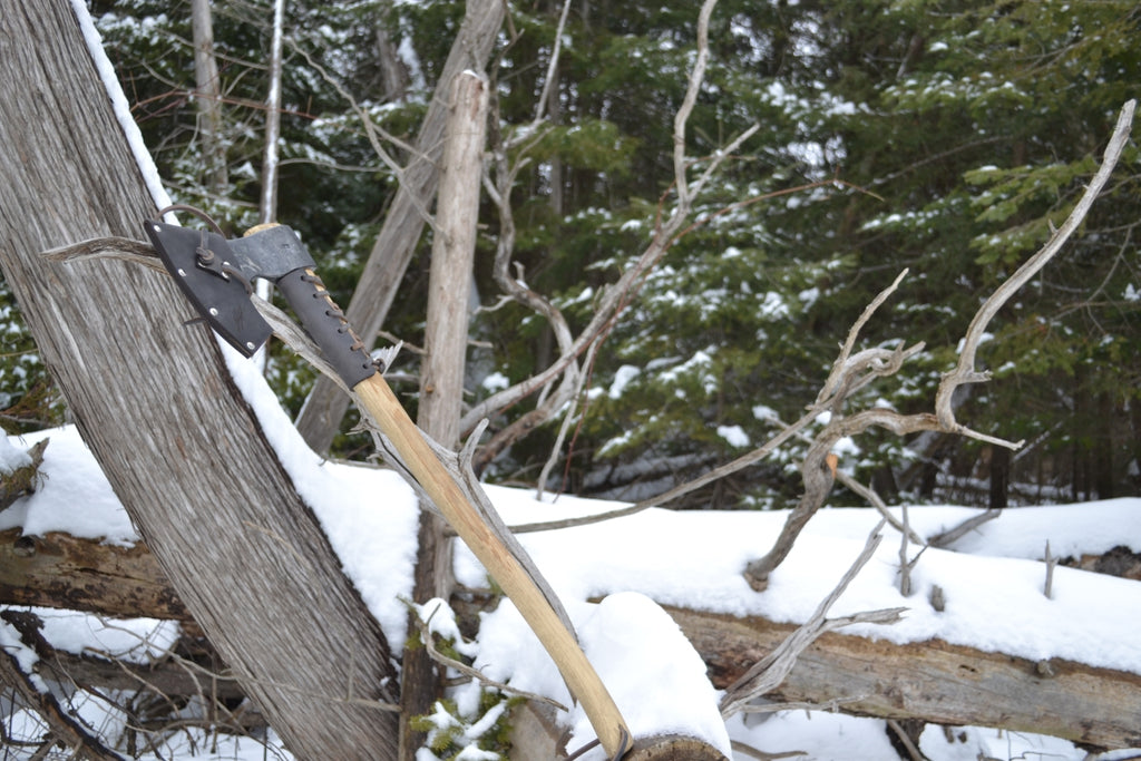 Taiga Moose bushcraft axe with natural hickory handle leaning against tree in snowy forest showing field-tested winter survival tool