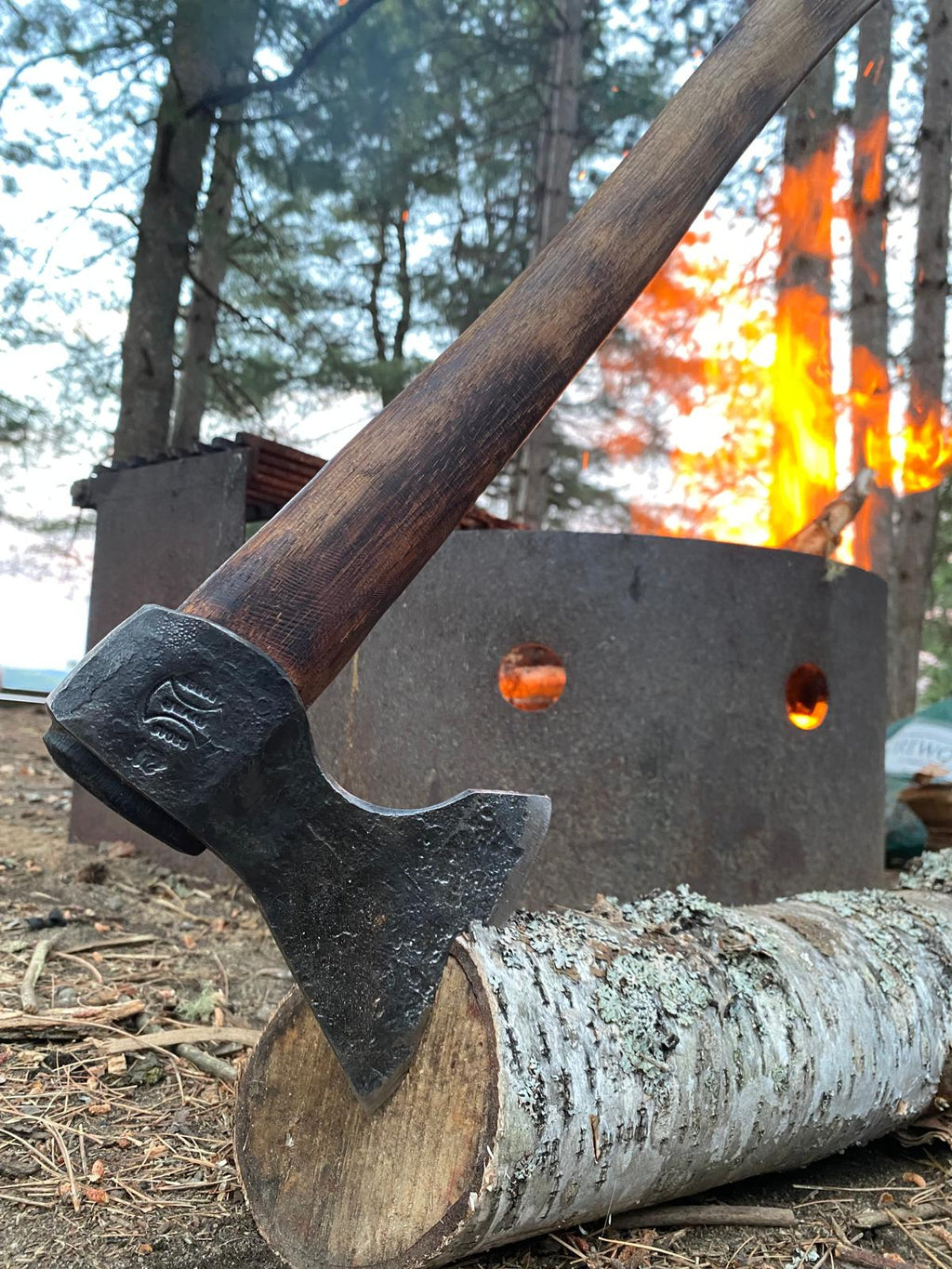 Hand-forged Taiga Wolverine axe by Broad River Forge stuck in log near campfire demonstrating real-world wilderness use